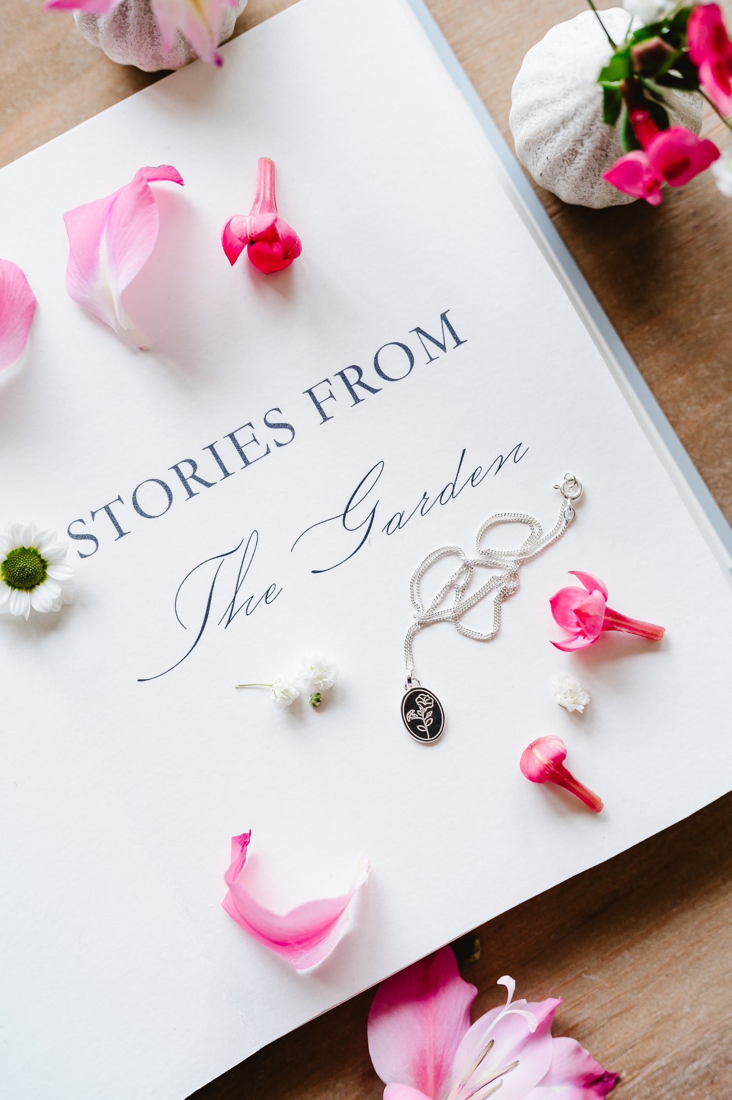 A dainty sterling silver necklace with a morning glory flower lying on an open book. Flowers in the background. 
