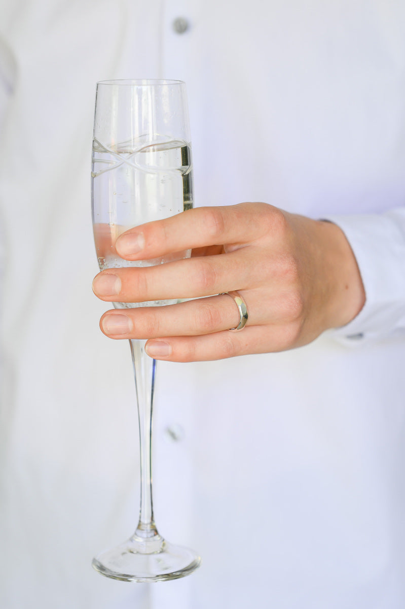 Sterling Silver Wedding Band with carved detail, Rock Ring, being worn by hand holding a champagne flute