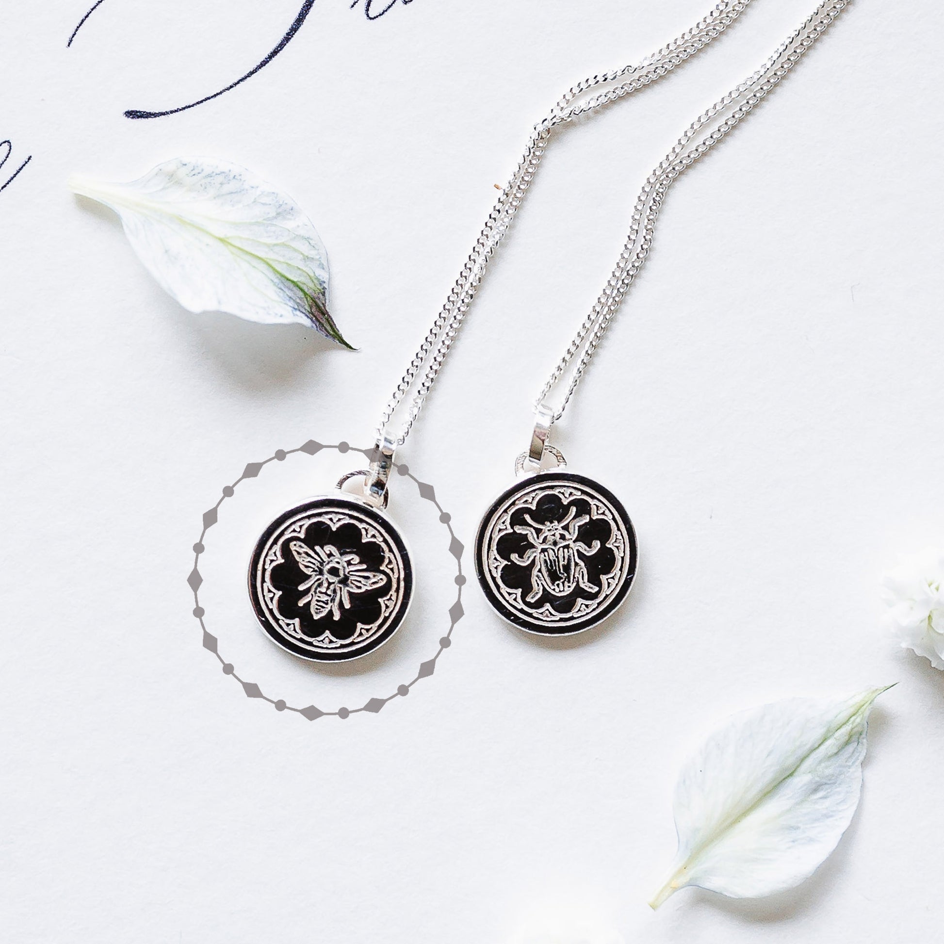 Two sterling silver necklaces, one with a bee and one with a beetle, both with a delicate border.