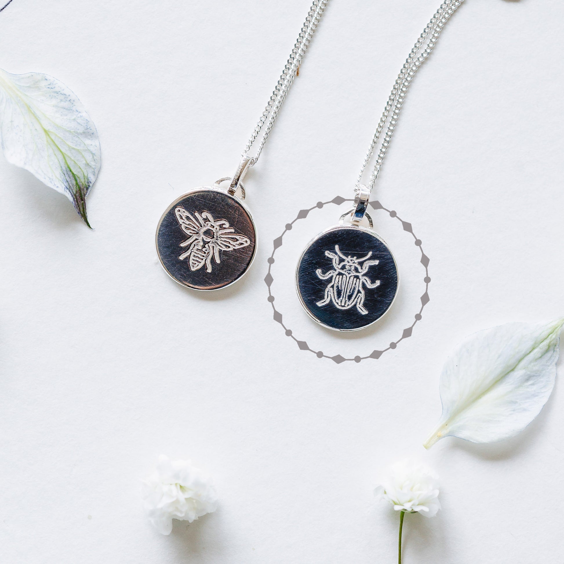Two sterling silver necklaces with bees and beetles, lying on a book page