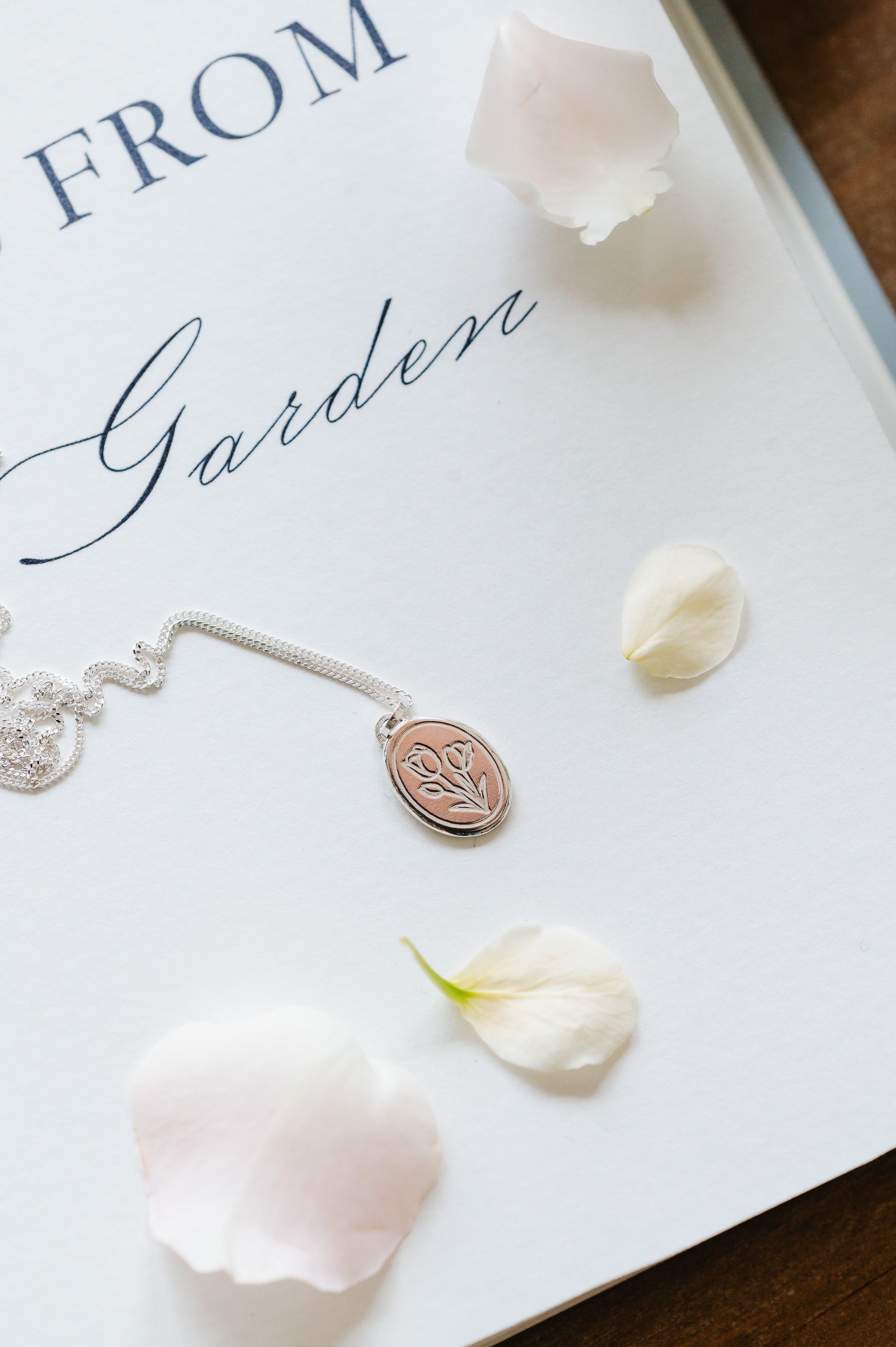 A sterling silver tulip necklace laid out on a flat surface with a few petals around it.