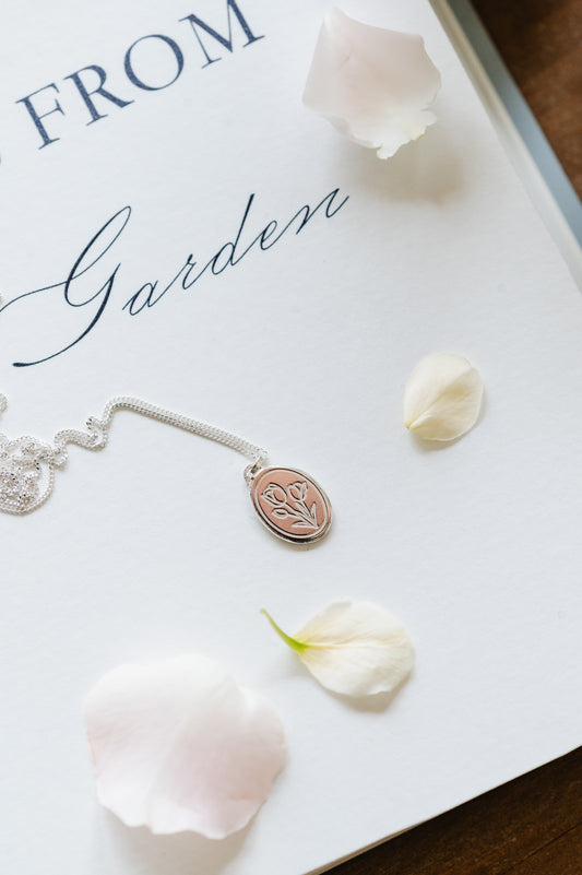 A sterling silver tulip necklace laid out on a flat surface with a few petals around it.