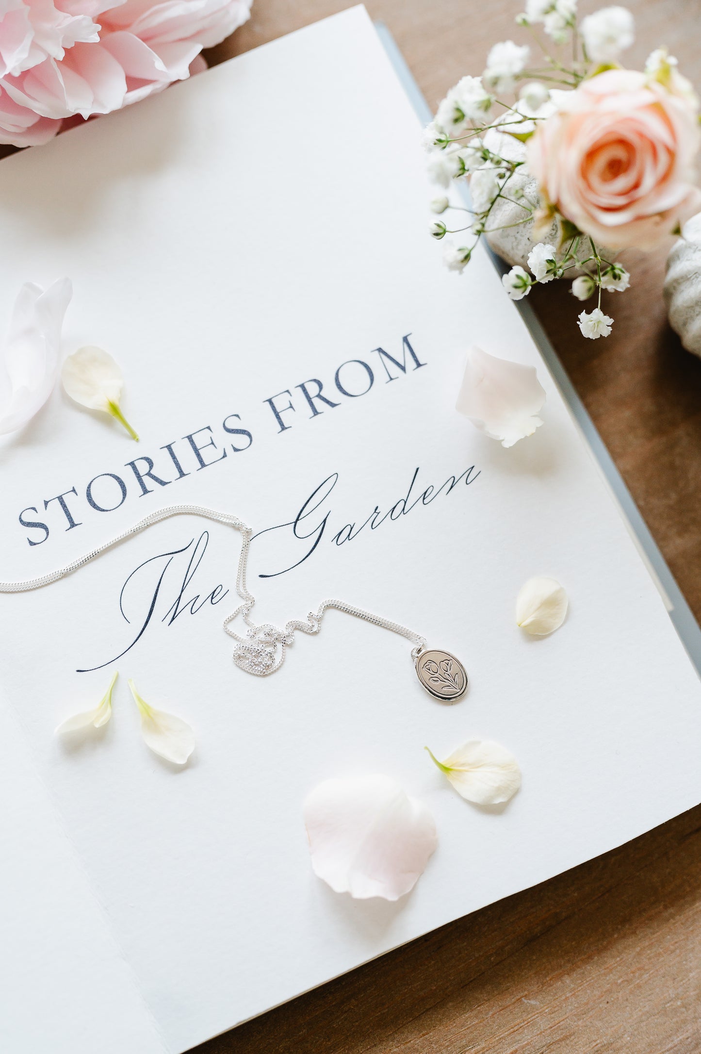 A sterling silver flower necklace with a tulip lying on an open book. Flowers in the background.