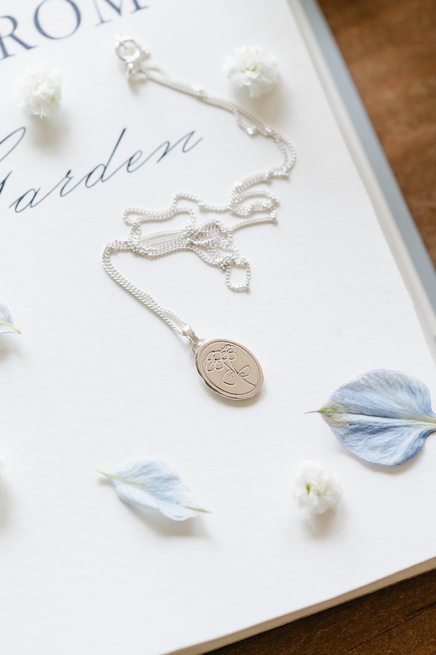 A sterling silver necklace with a violet/pansy flower and heart-shaped leaves, displayed on a book with a white background.