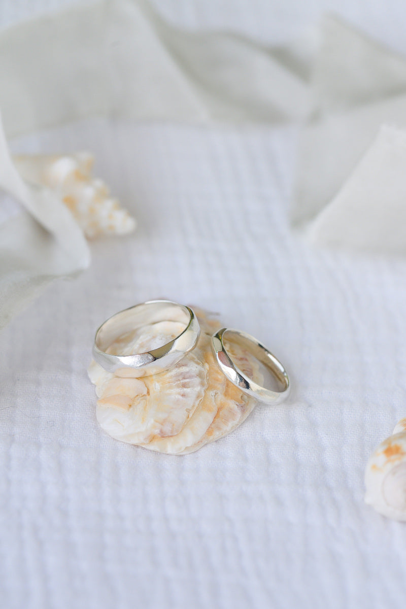 Two silver wedding rings on a white fabric background with seashells.