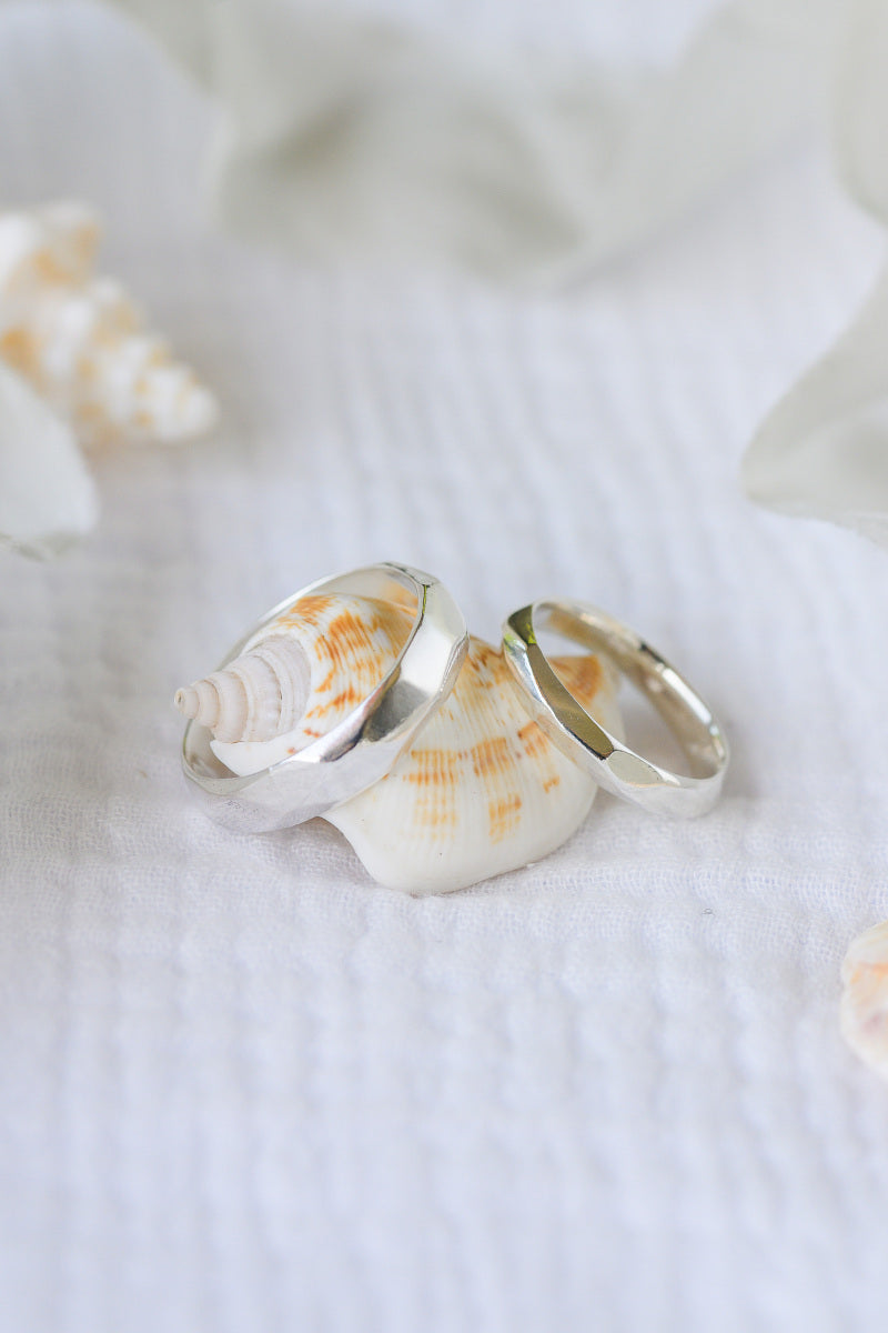 Carved silver wedding rings leaning on seashells.