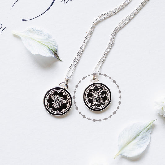 Two dainty sterling silver necklaces, one with a beetle one with a bee. The delicate necklaces are lying on a white page with petals.