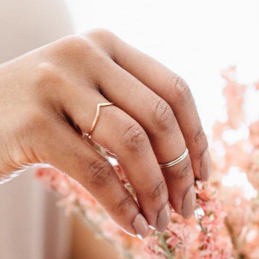 A hand wearing a thin rose gold wishbone and a pair of silver mid rings. 