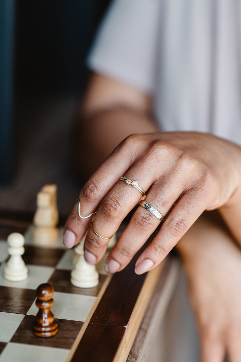 Recycled 18ct white gold hammered wedding band, a pair of stacking stone set rings. Rings being worn by a hand holding a chess piece