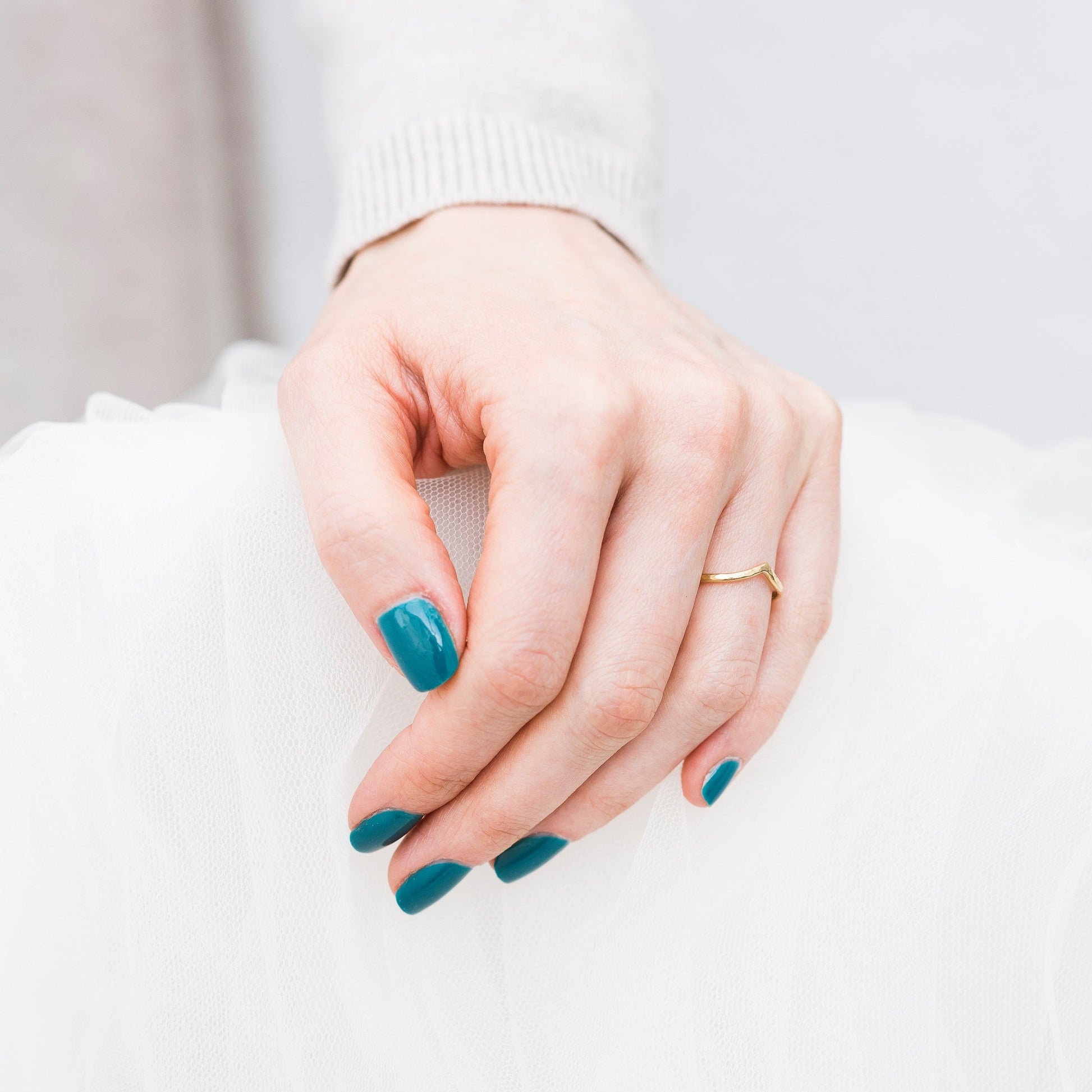 18ct yellow gold wishbone ring, worn on a hand with blue nail polish