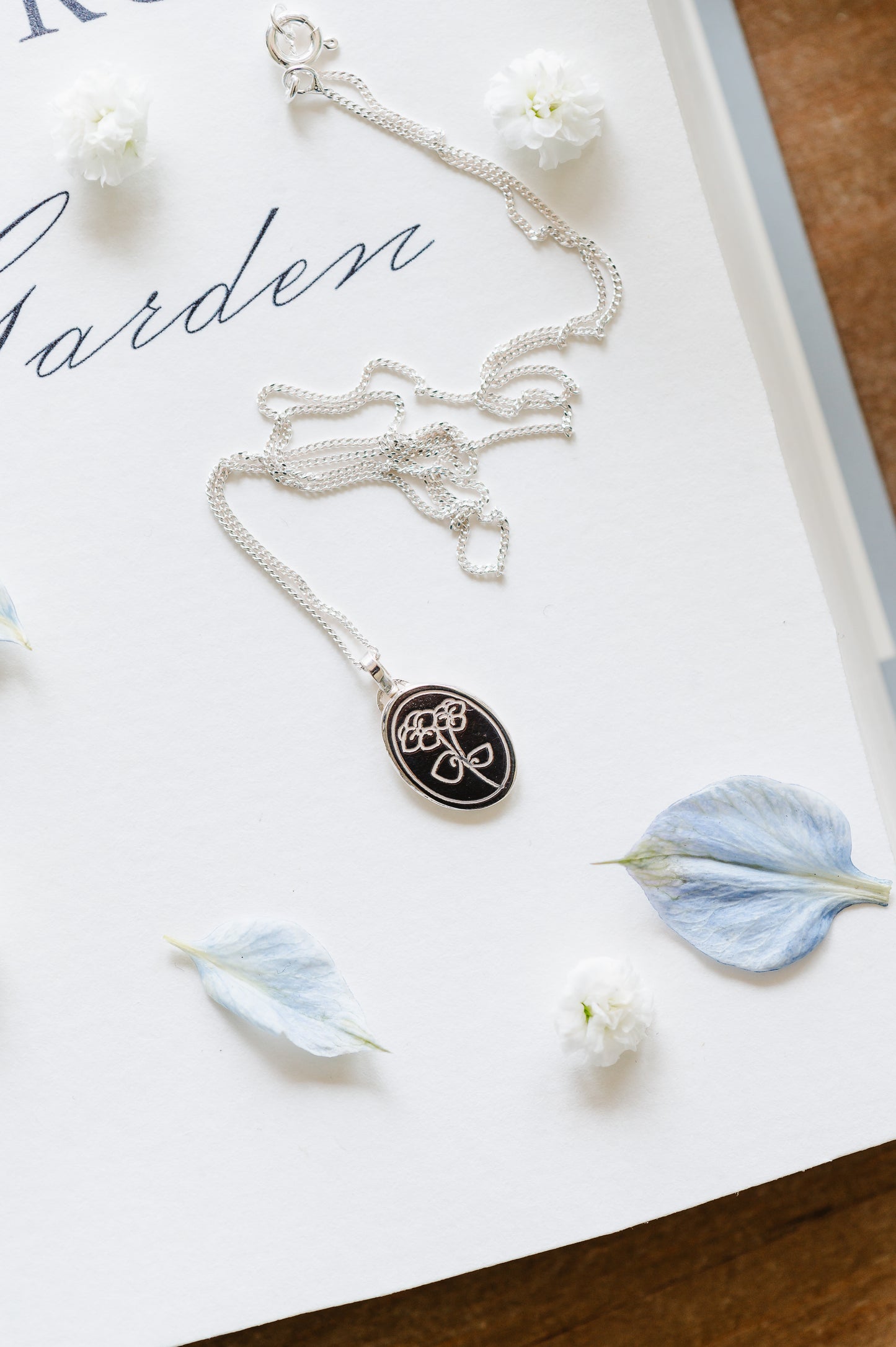 sterling silver necklace with violet flower, pansy flower necklace, lying on a book page with petals
