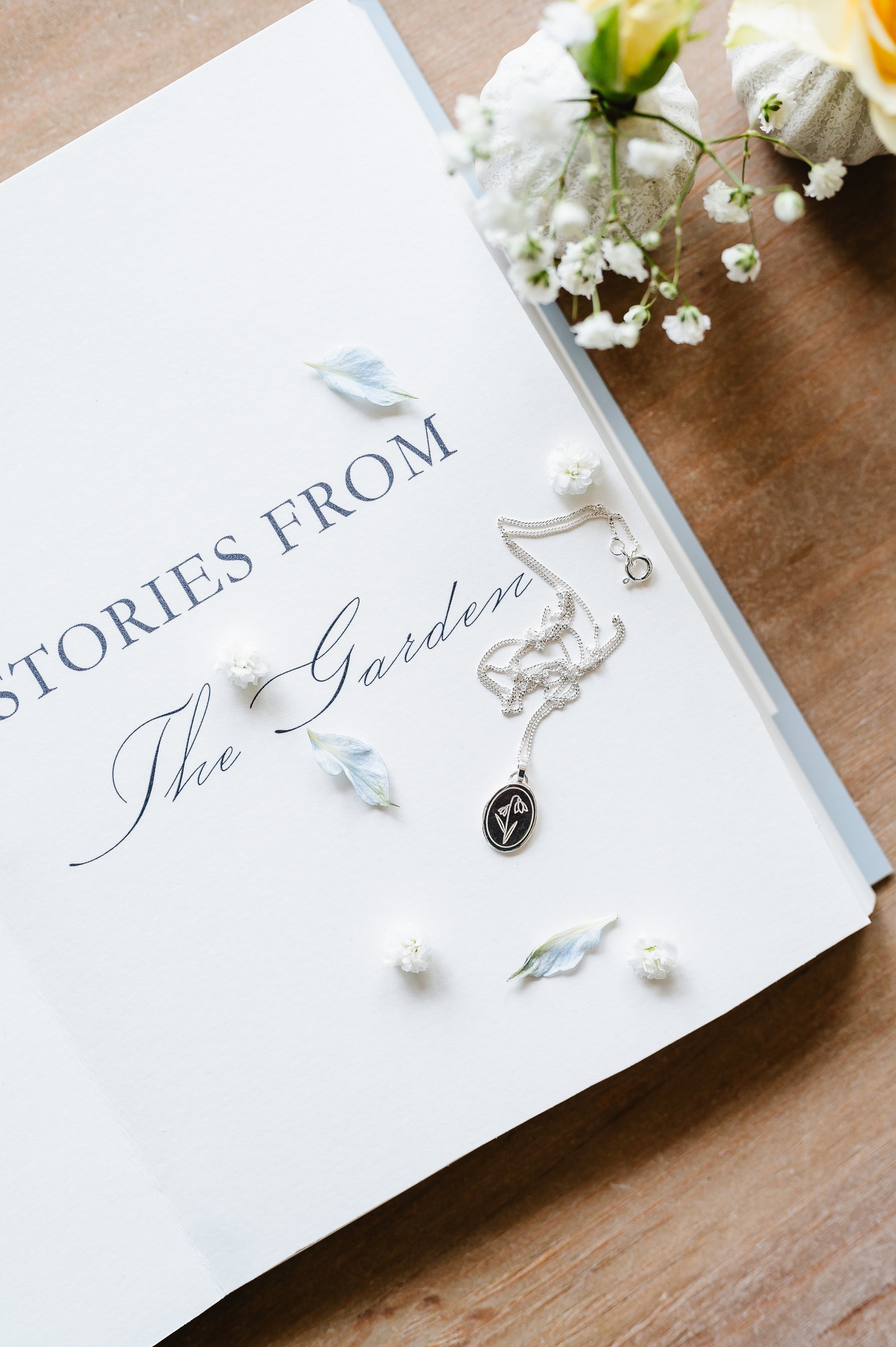 a sterling silver necklace with a snowdrop flower, shown lying on an open book.