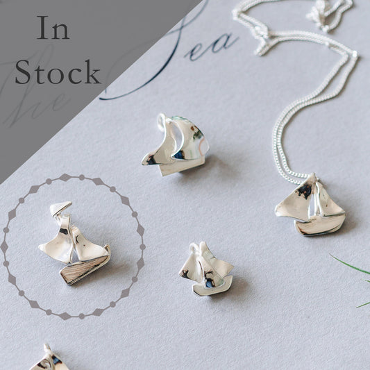 Solid sterling silver sailing boat necklace with a focus on its detailed design. The necklace is displayed on a grey background with the text 'In Stock' and 'Sea' visible in the backdrop.