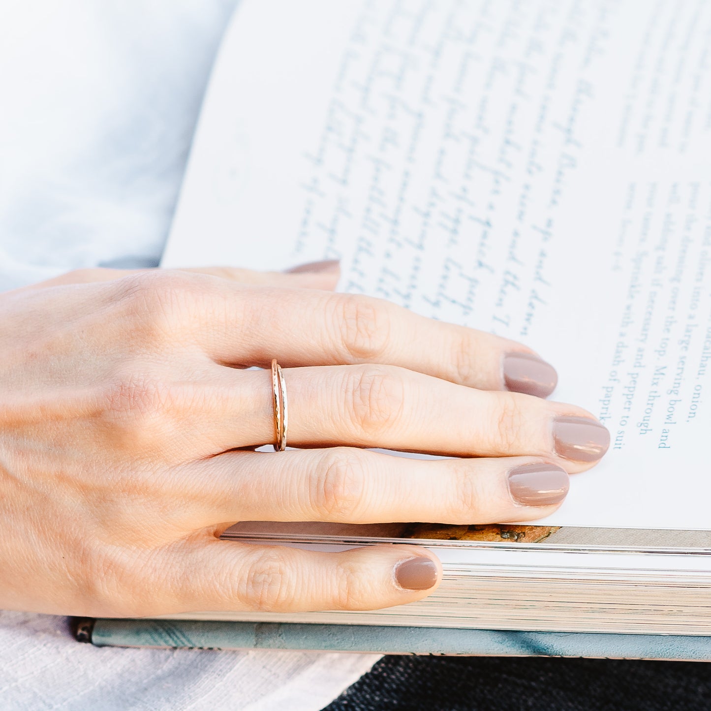 A pair of joined or russian wedding ring style bands in 9ct white and rose gold, with a hammered finish. Hand resting on a book