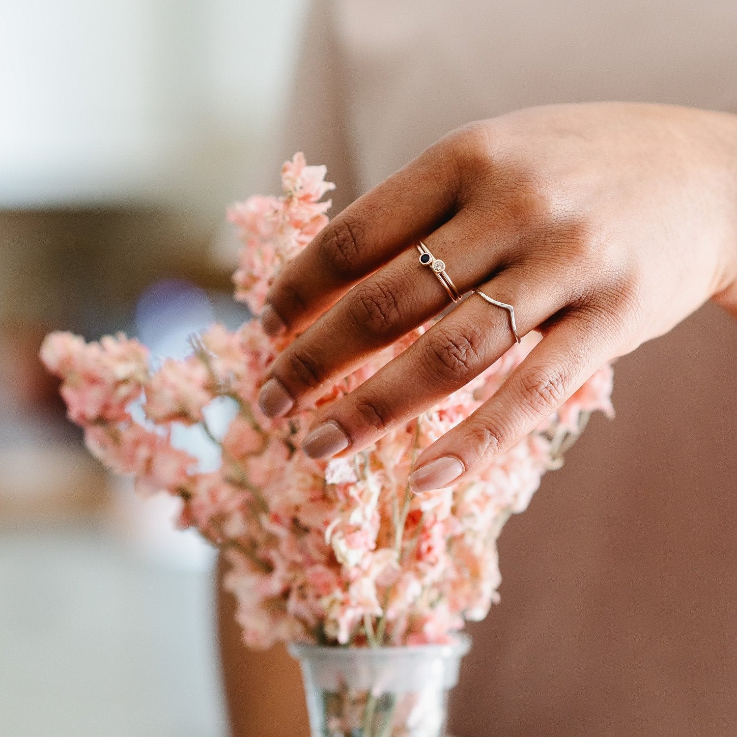 Slim 9ct white gold wishbone wedding ring. A simple wishbone ring being worn, with a couple of stone set rings on a hand arranging some flowers.