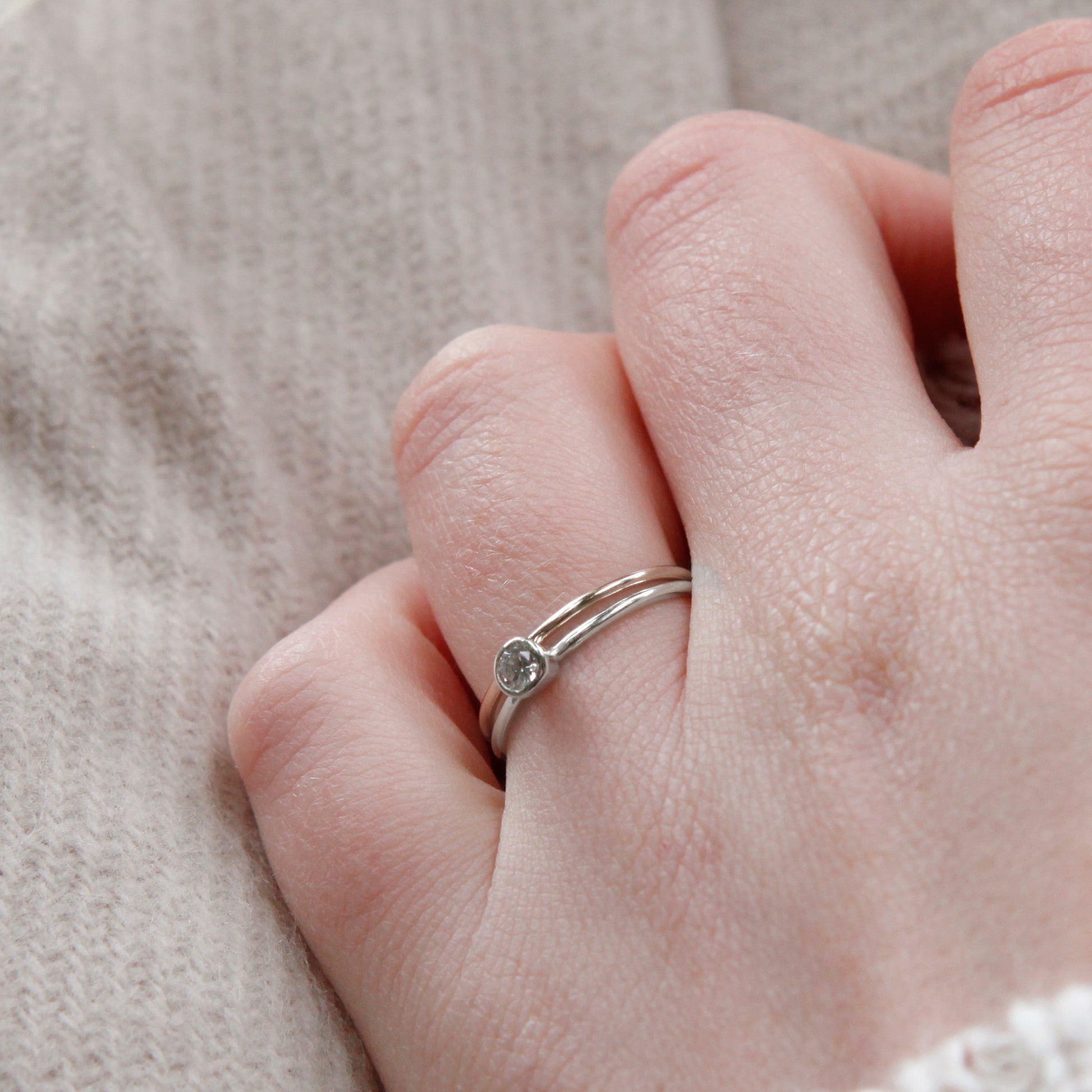 A pair of rings, one with a stone being worn, hand leaning against a beige scarf