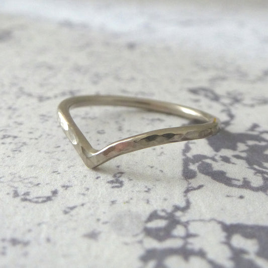 A white gold wishbone-shaped ring with a hammered texture, placed on a patterned surface.