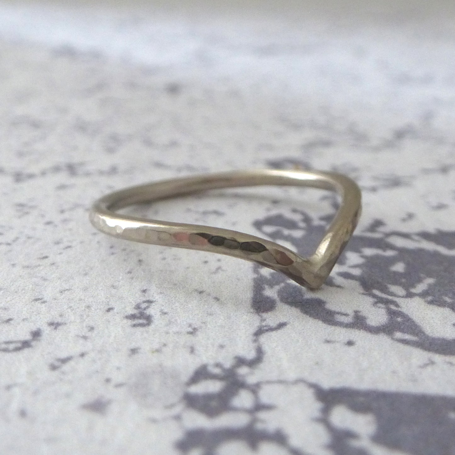 18ct white gold wishbone wedding ring, sitting on marbled paper. 