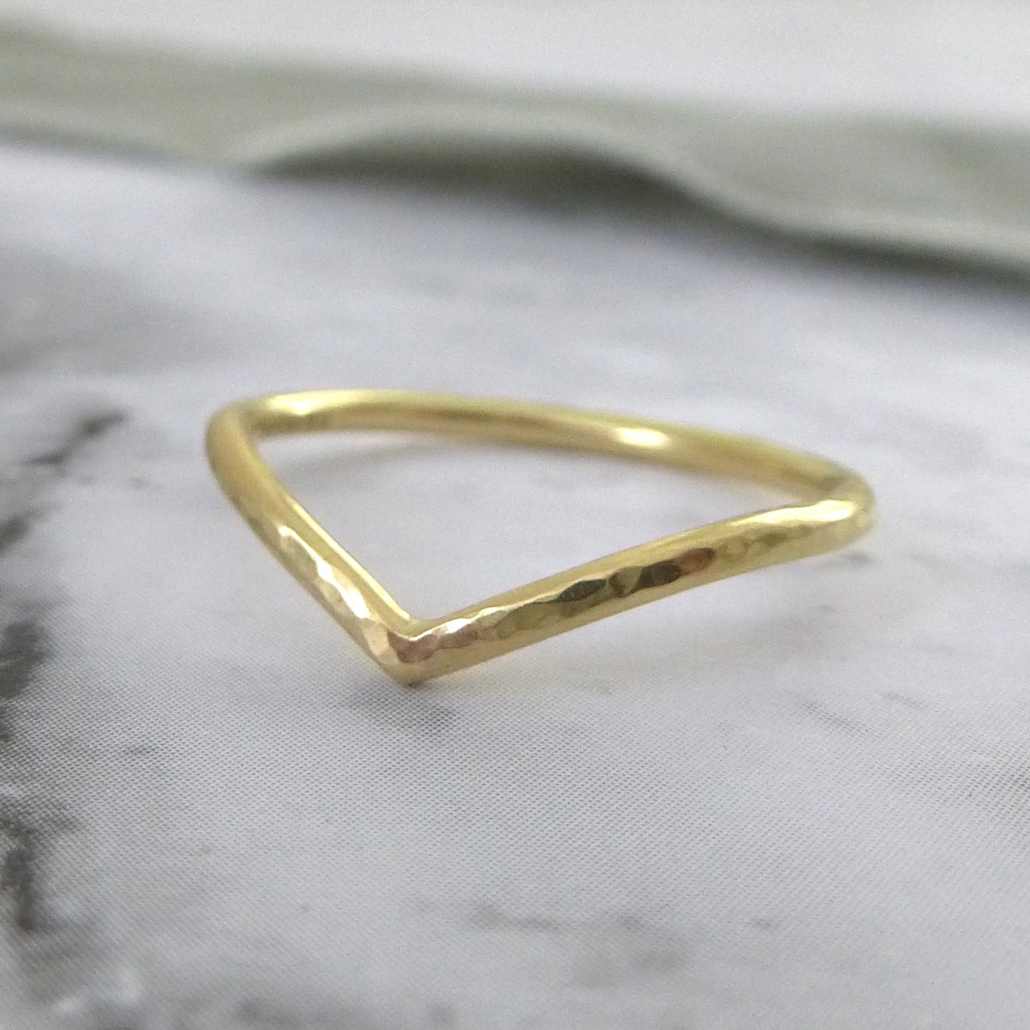A hand-shaped 18ct gold wishbone ring with a subtle hammered texture, displayed on a grey background.