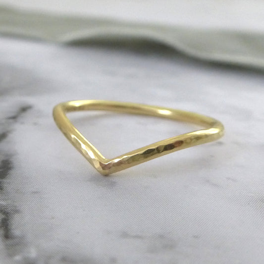 A hand-shaped 18ct gold wishbone ring with a subtle hammered texture, displayed on a grey background.
