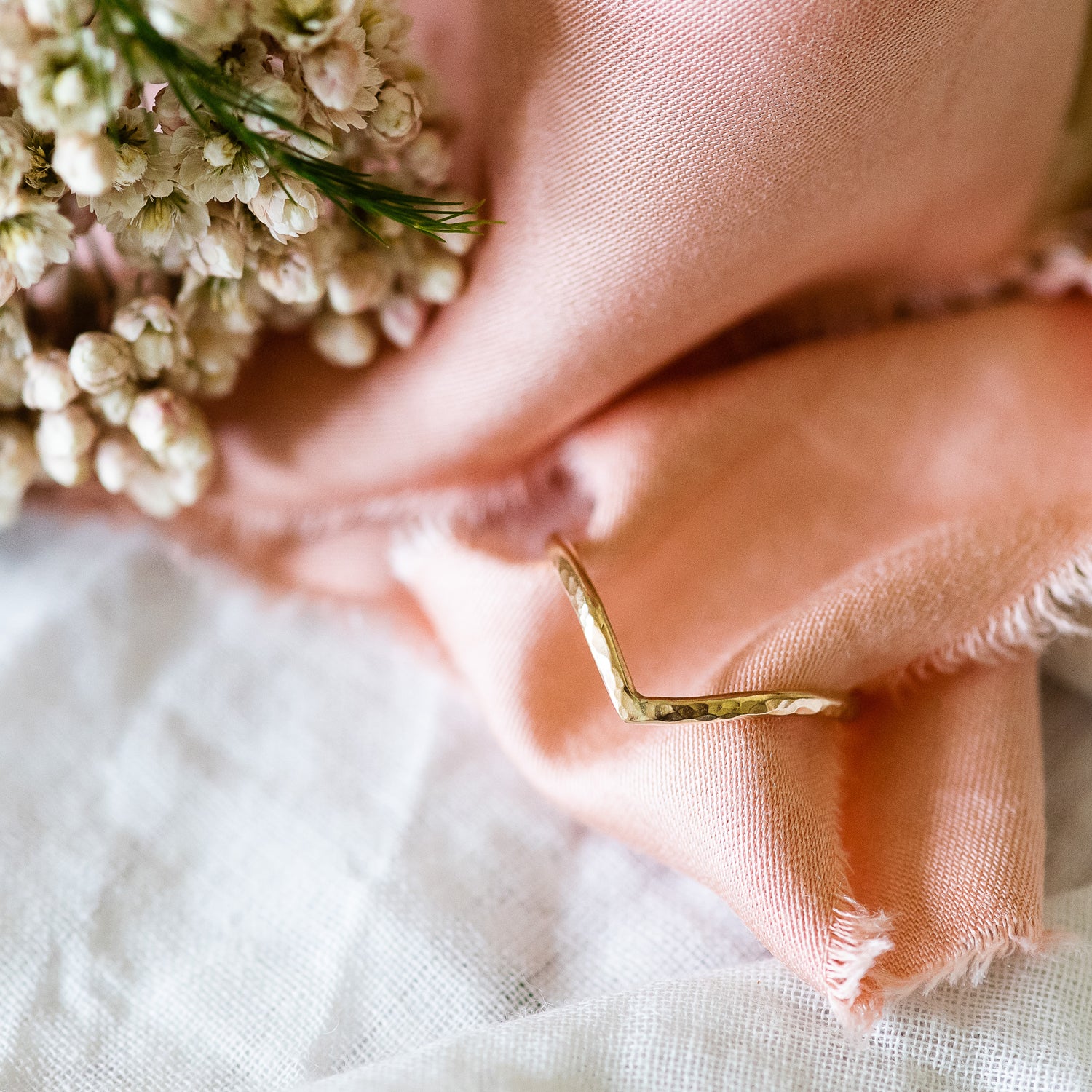 18ct gold wishbone wedding ring, balanced on a ribbon, with rice flowers in the background