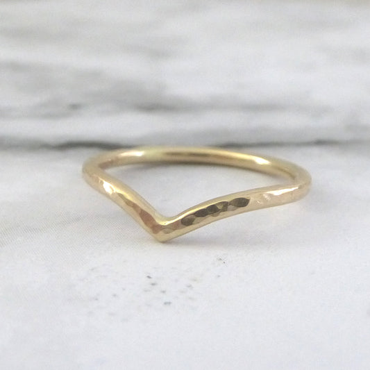 A subtle yellow gold wishbone ring with a hammered texture, displayed against a marble paper background.