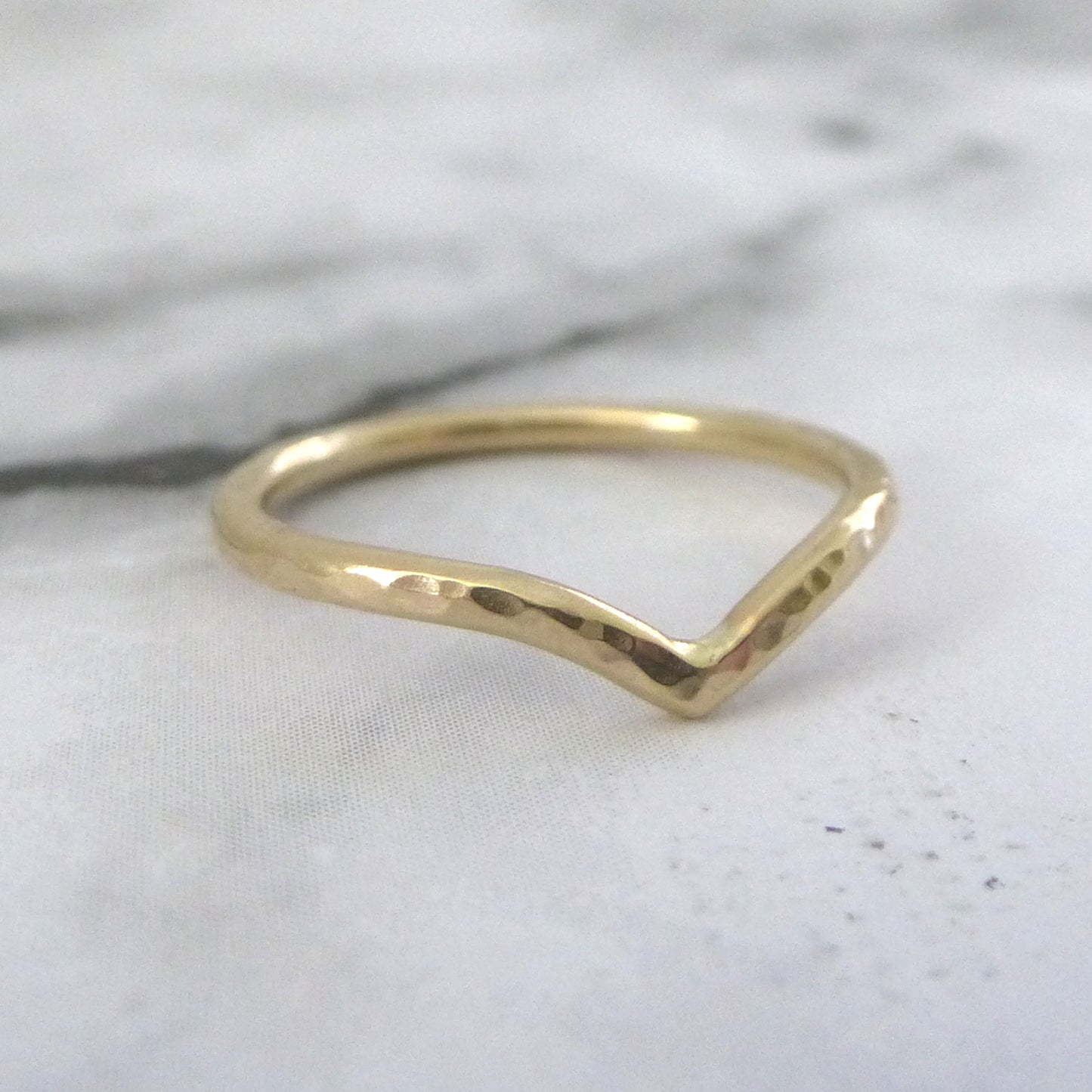 A 9ct gold wishbone ring, hammered, sitting on marble paper