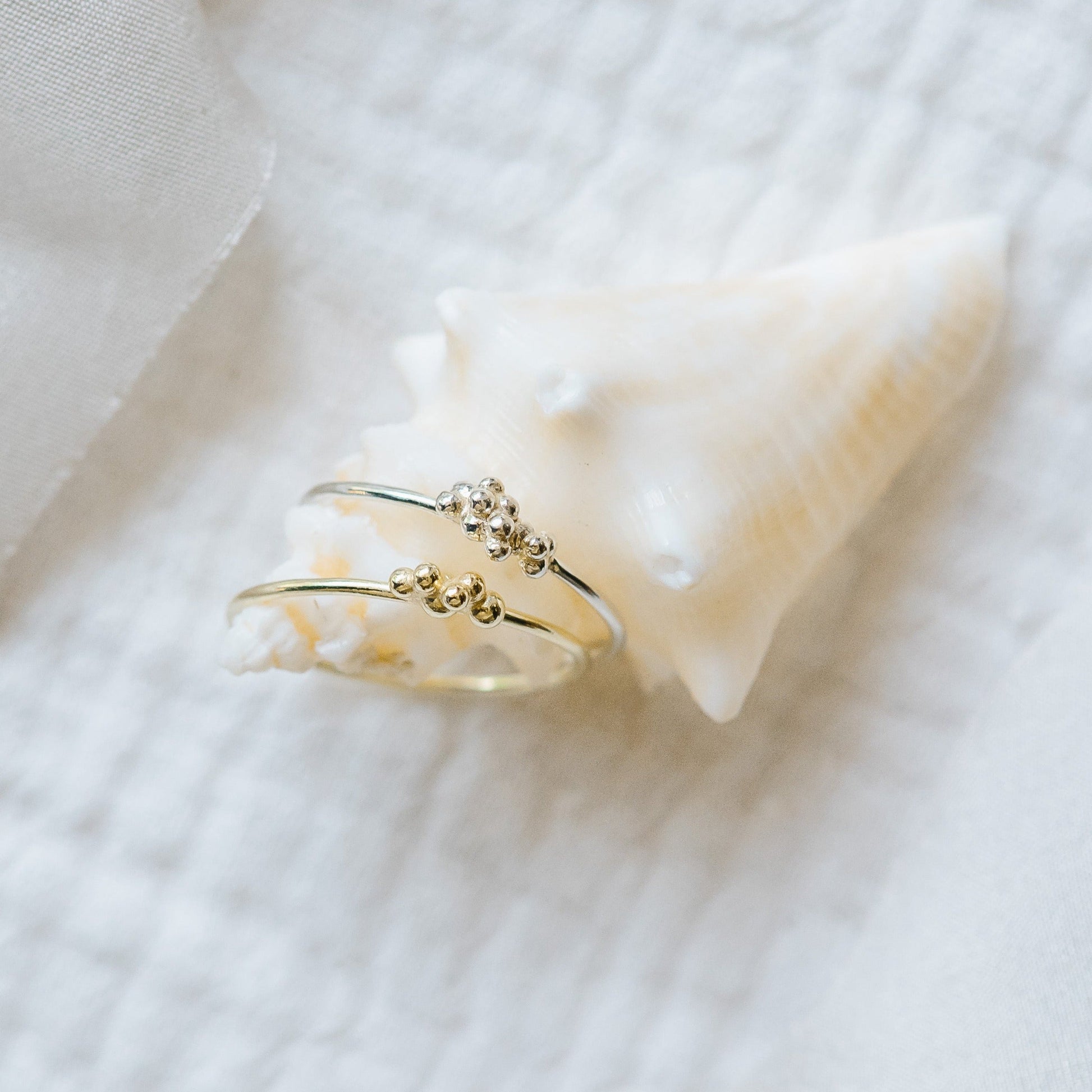 A pair of thin rings with bubbles of solid gold and silver, balanced on a seashell.