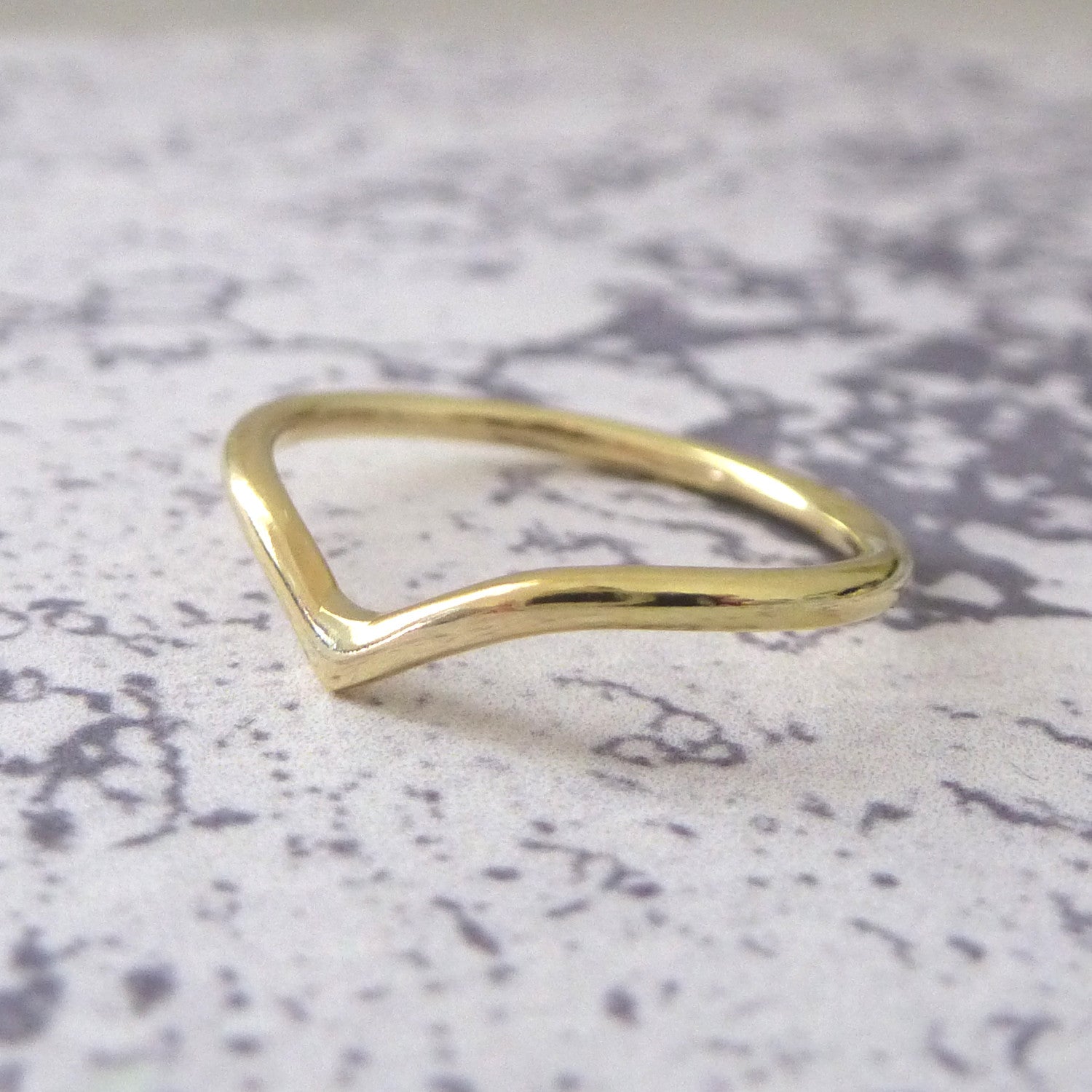 An 18ct gold wishbone wedding ring, sitting on a marbled background.