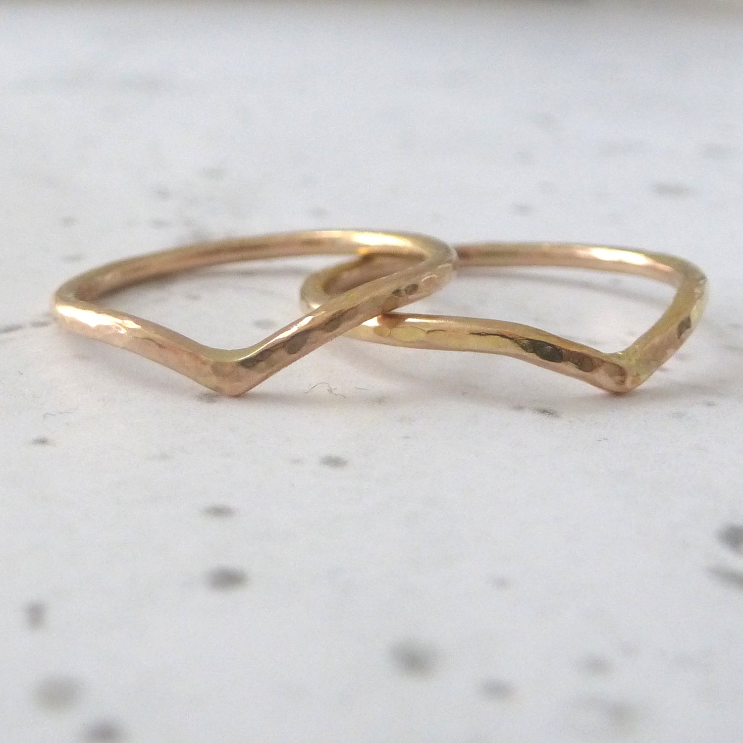two 18ct rose gold wishbone rings, sitting on a marbled paper background.