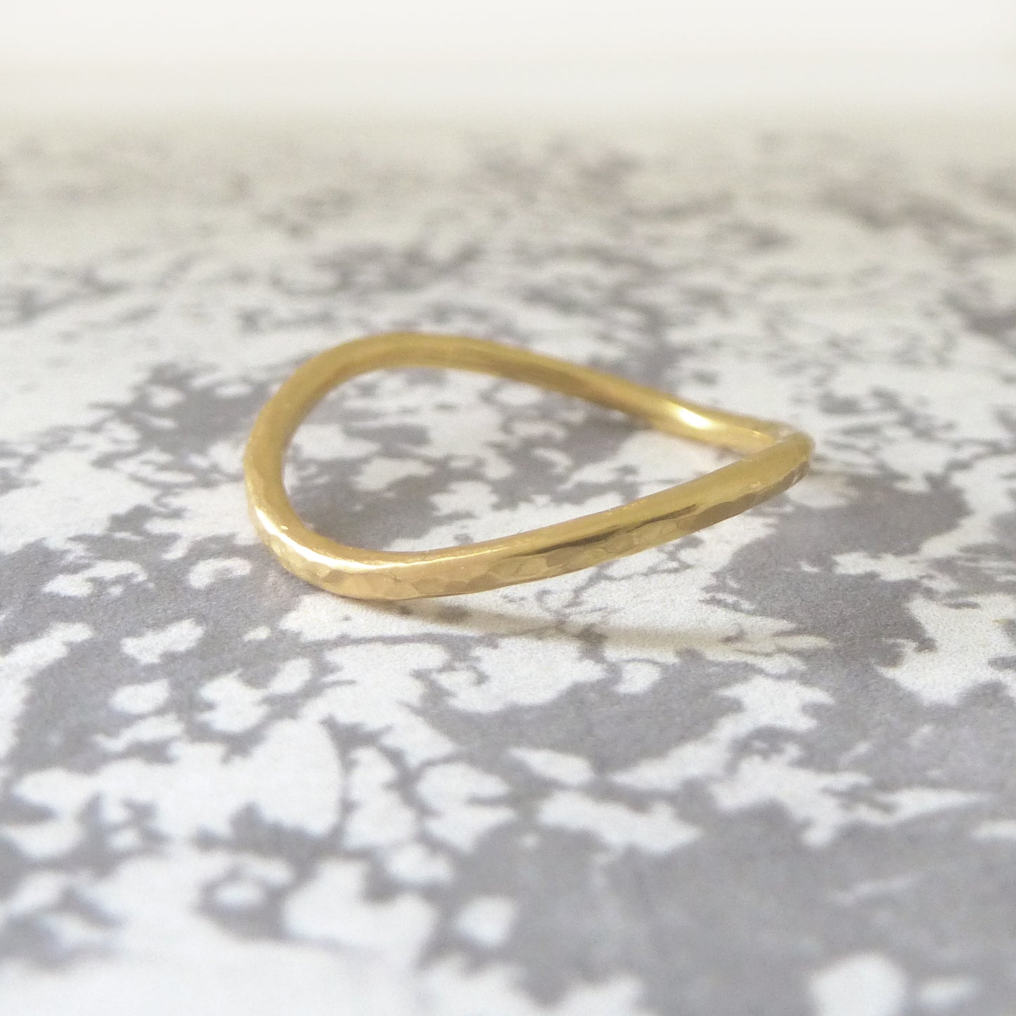 An 18ct yellow gold curved band with hammered finish on a marble paper background.