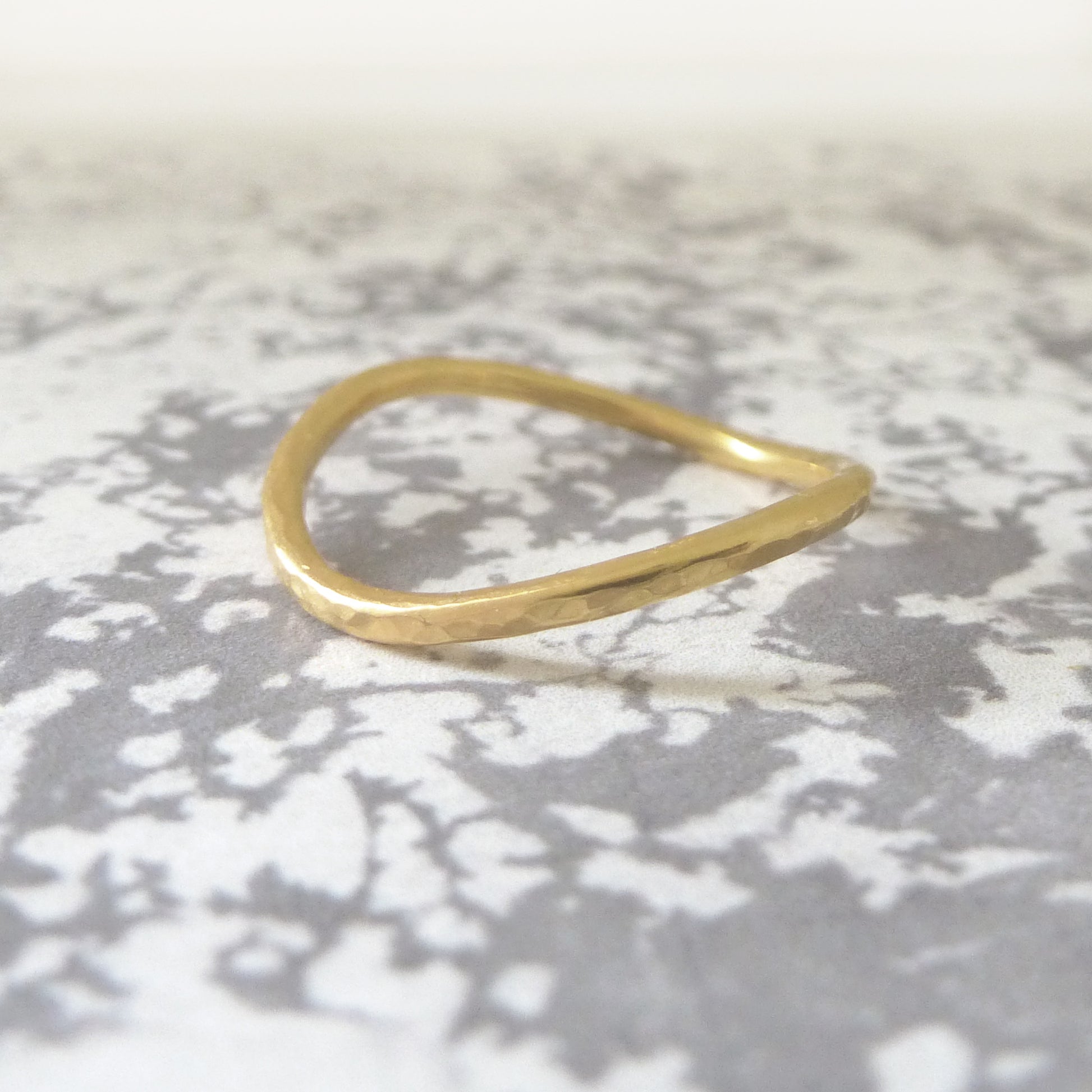 An 18ct yellow gold curved band with hammered finish on a marble paper background.