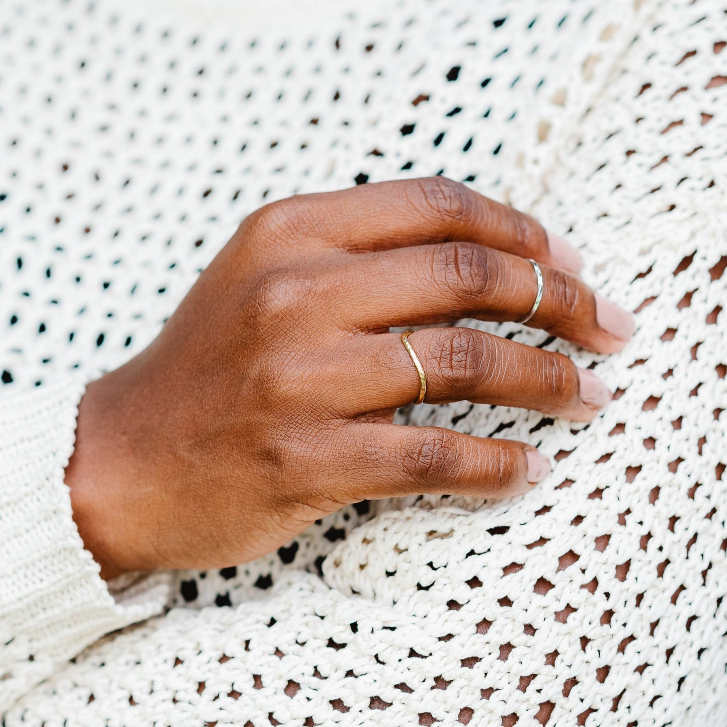 18ct yellow gold hammered curved ring being worn against a cream crochet jumper