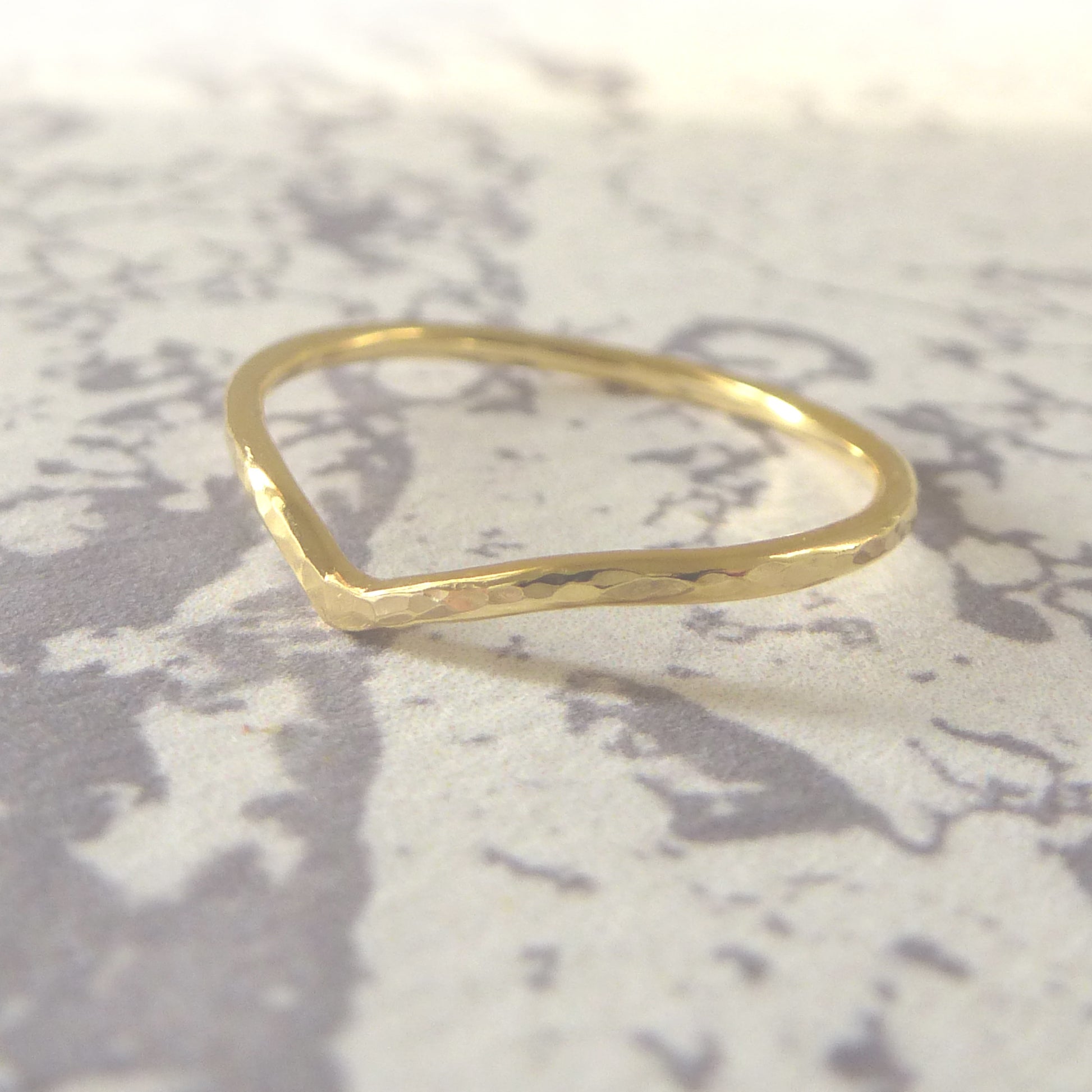 A gold wishbone ring with a smooth finish, displayed on a textured grey background.