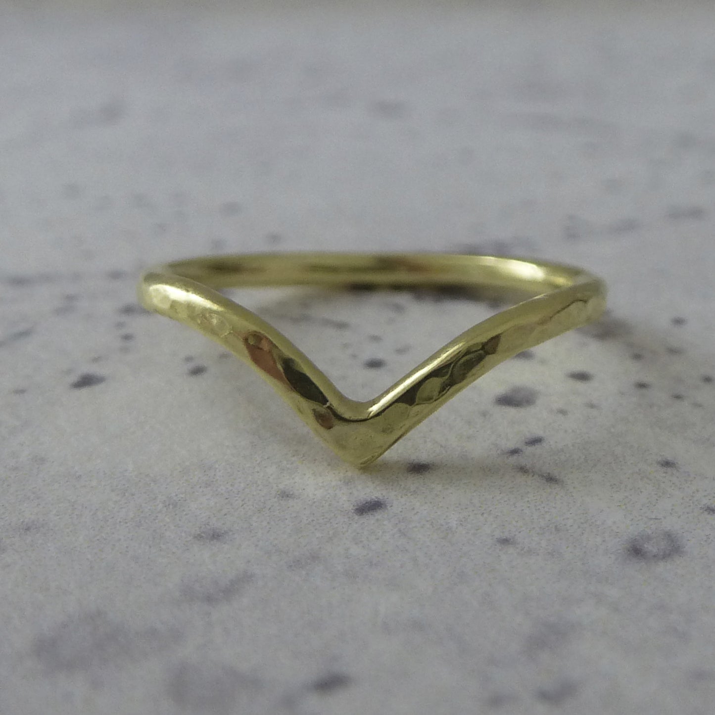 An 18ct gold wishbone wedding ring, sitting on marbled paper.