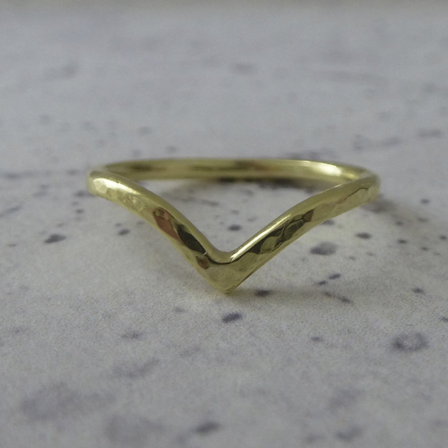 An 18ct gold wishbone wedding ring, sitting on marbled paper.