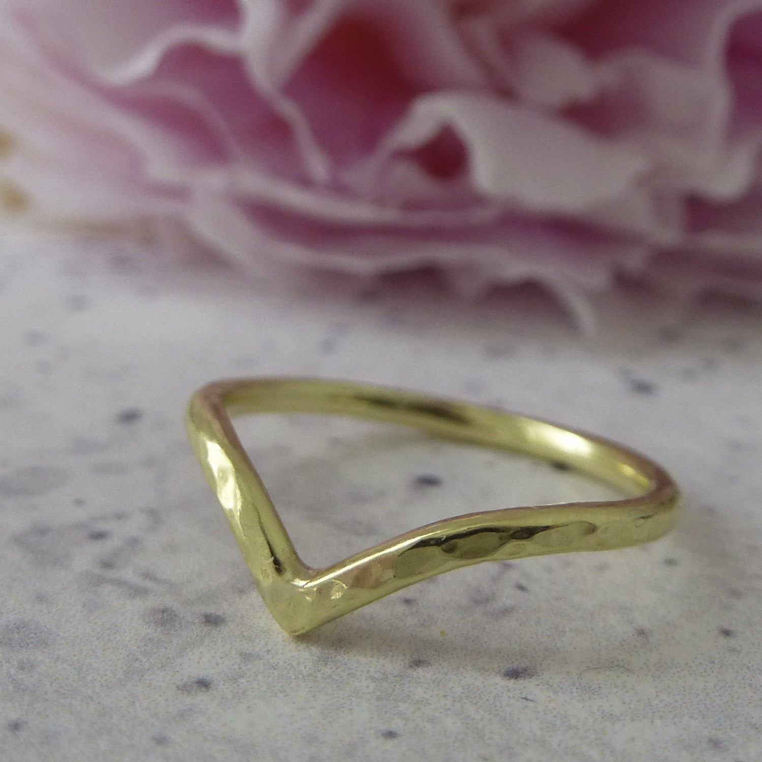An 18ct yellow gold wishbone ring with a hammered finish, sitting on marbled paper.