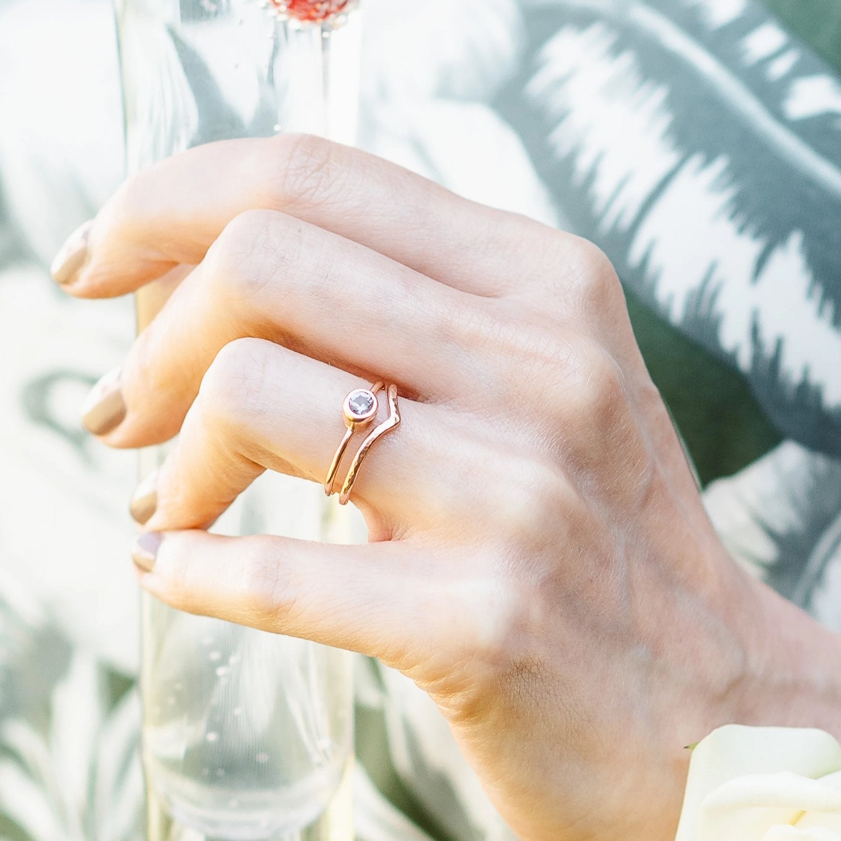 A hand holding a glass, wearing a spinel ring and 9ct rose gold wishbone ring set