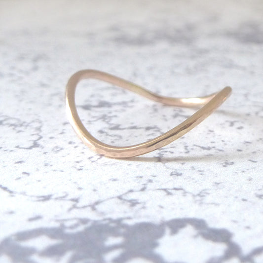 A rose gold rocking wishbone ring with a smooth finish, displayed on a textured background.