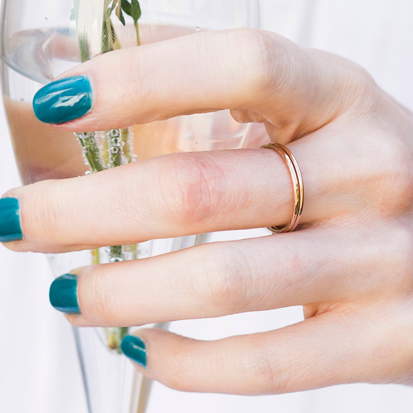 A pair of 9ct rose gold bands being worn by a hand holding a champagne flute