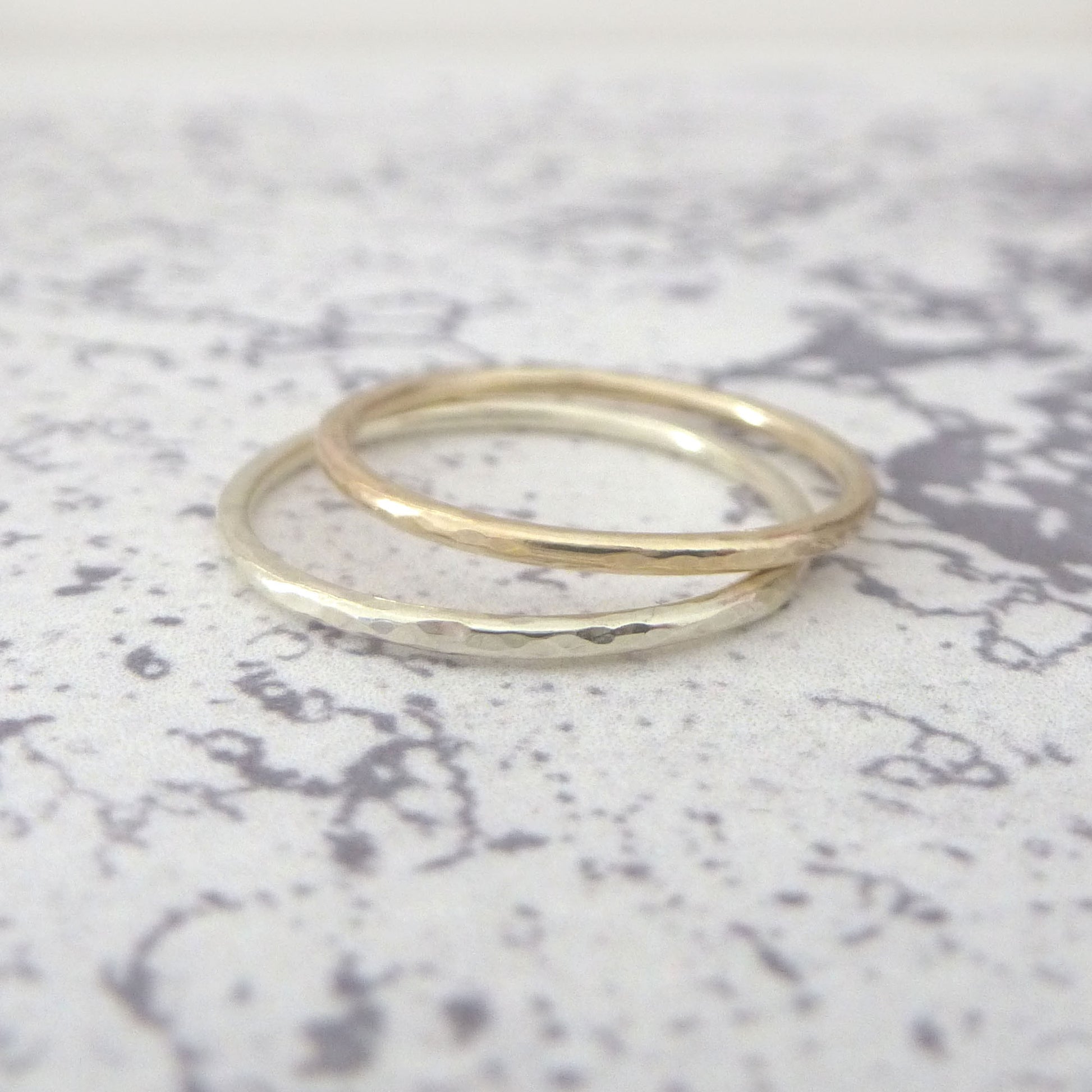 Two 9ct gold rings, one with a hammered texture and the other with a smooth finish, lying on a speckled background.