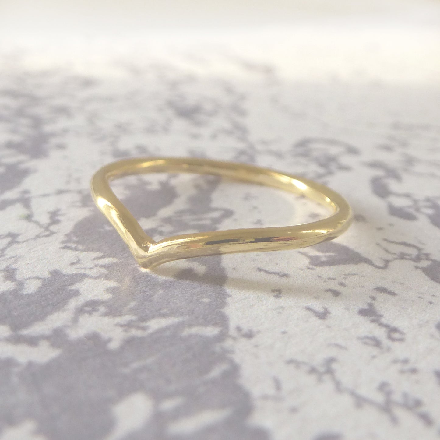 18ct yellow gold wishbone wedding ring, smooth finish, sitting on a marbled background.