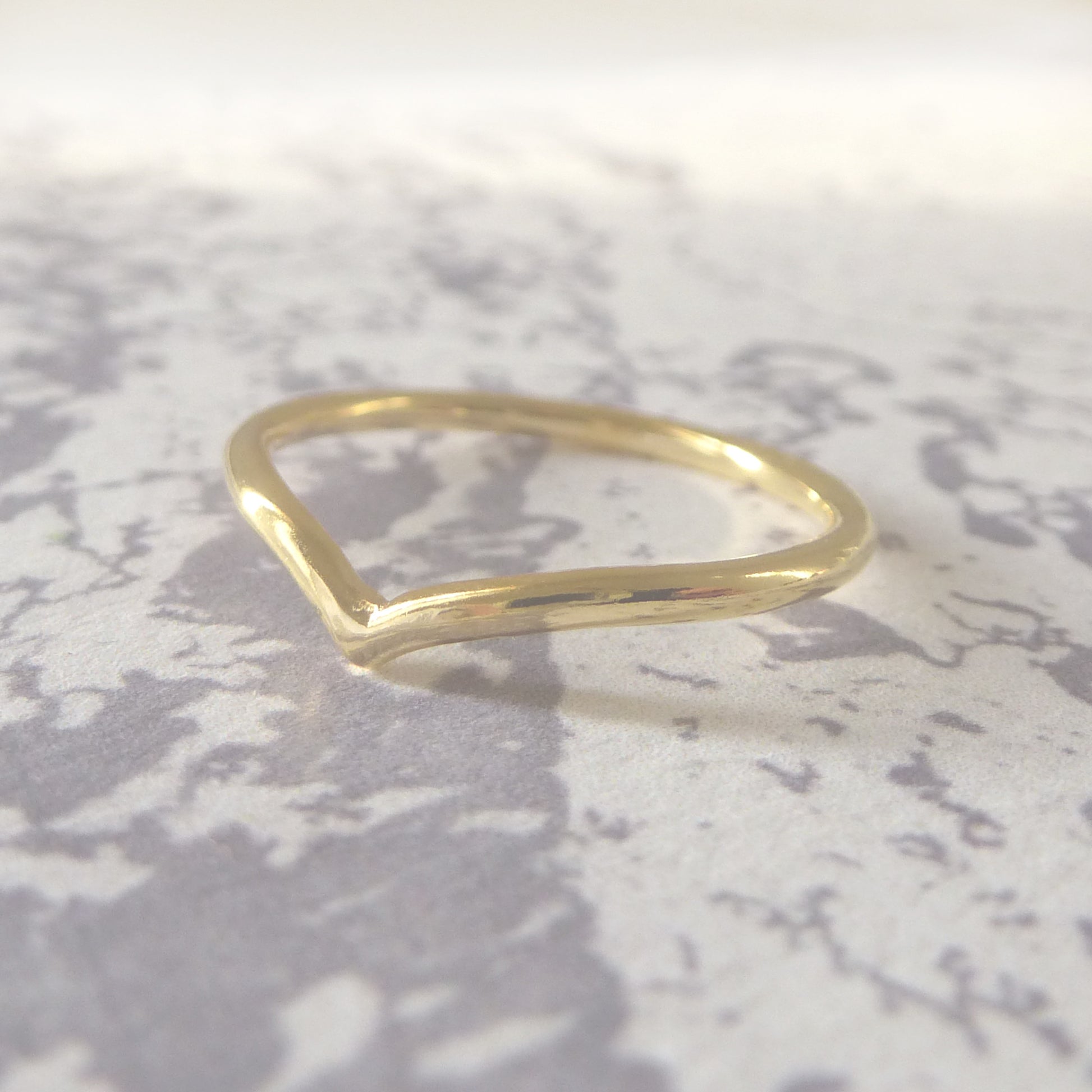 18ct yellow gold wishbone wedding ring, smooth finish, sitting on a marbled background.
