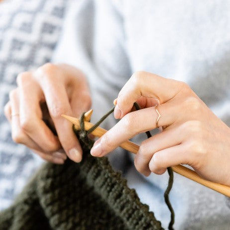 A woman knitting, wearing a thin wishbone ring