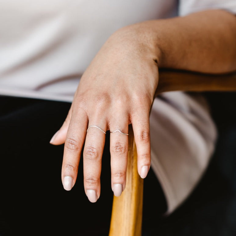 A hand wearing two thin rings, one wishbone ring and one curved band