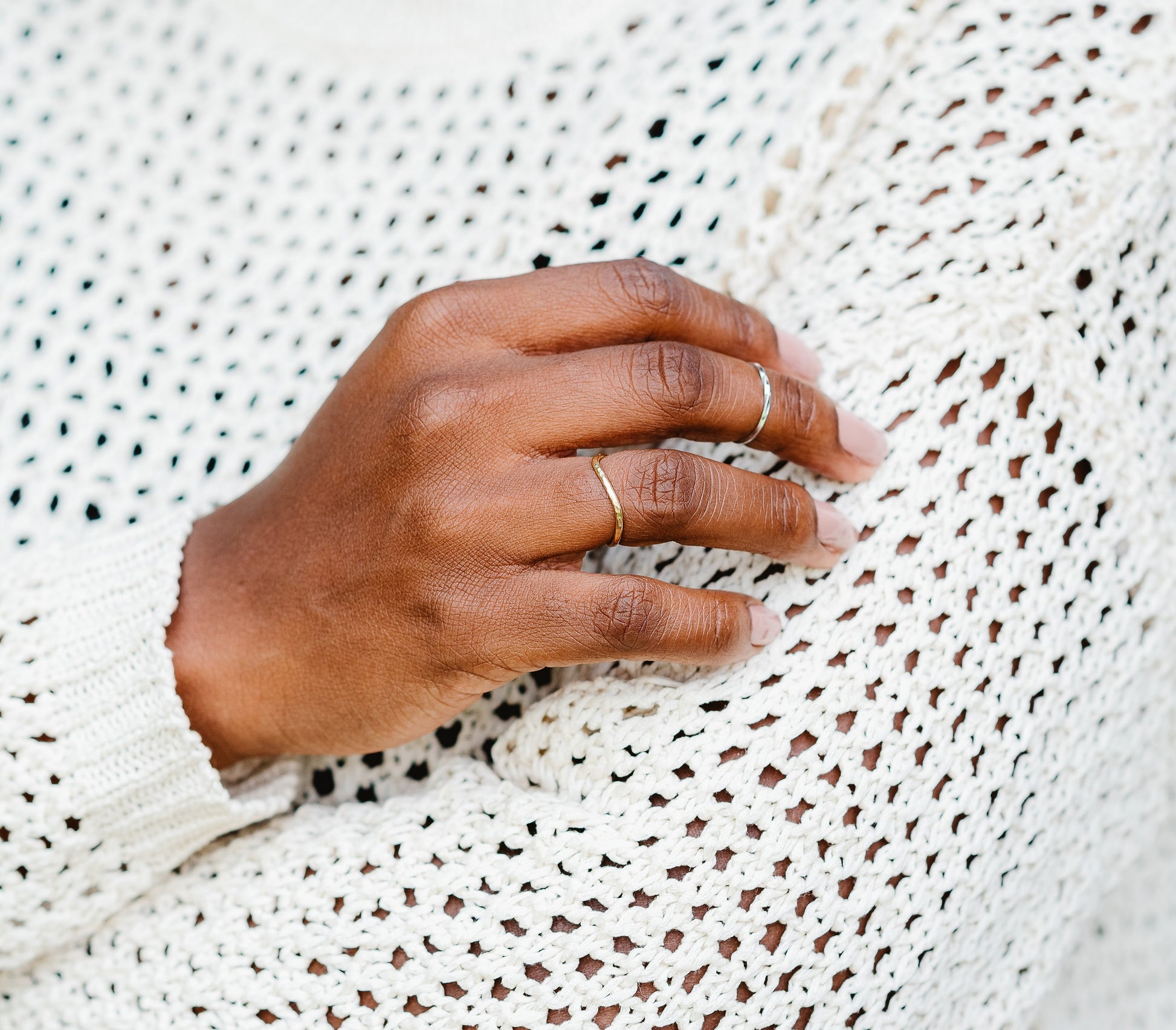 A hammered curved ring being worn, hand against a cream crochet jumper