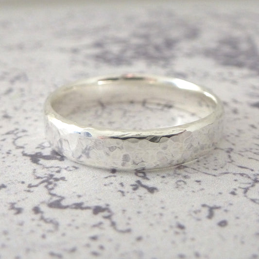 A hand-shaped band ring in sterling silver with a hammered finish, displayed on a textured background.