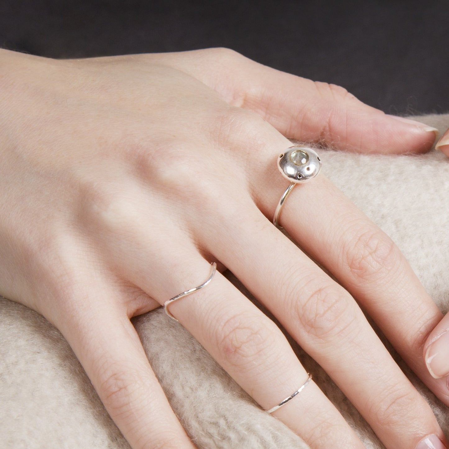 A hand resting on a cosy rug, wearing some sterling silver rings