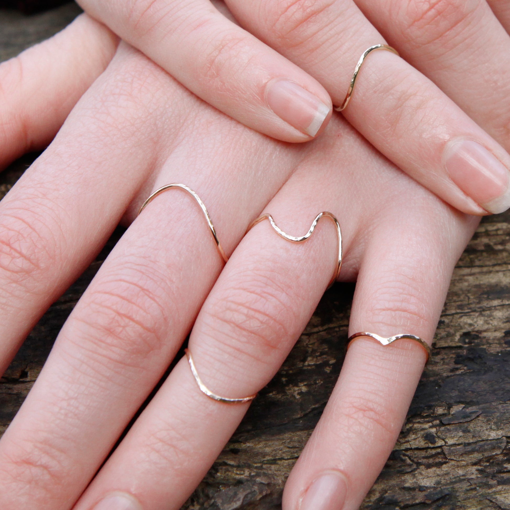A selection of thin gold rings, hand leaning on some bark