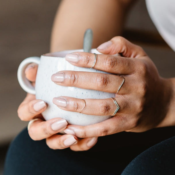 A hand wearing a selection of thin rings holding a mug